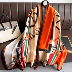 Detailed close-up of orange equestrian printed satin scarf draped on a leather couch