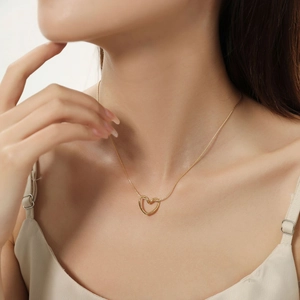 Dettaglio di una collana con ciondolo a cuore dorato indossata da una modella