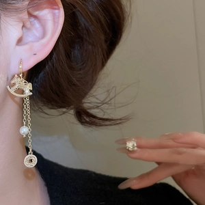 Détail de boucles d'oreilles poney dorées avec perle blanche et pompon de style chinois