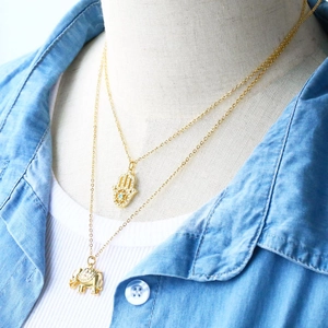 Detailed view of layered gold elephant necklace and Hamsa Hand pendant on a model