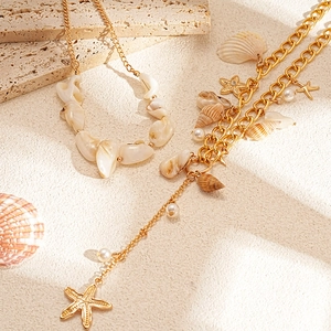 Golden starfish and shell necklace set with faux pearls on sandy beach background
