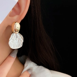Macro detail of gold and silver shell texture earrings worn by a model
