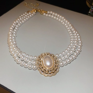 Close-up of triple-layer pearl necklace with a rhinestone oval gold pendant