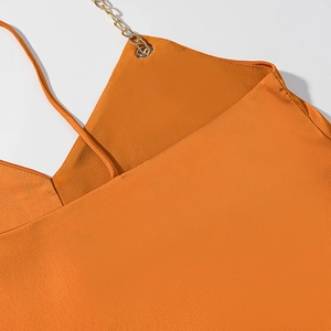 Dettaglio dell'abito in raso arancione con trama crepe ed elegante spallina a catena d'oro