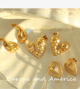 Detailed view of three golden earrings with heart and drop shapes on a shell tray