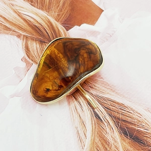 Macro detail of amber resin hair clip with gold metal frame worn on brown hair