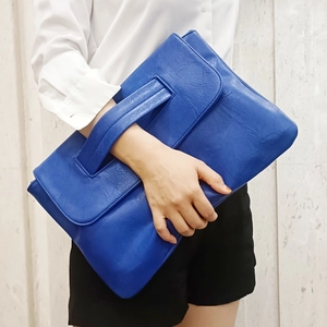 Detail of royal blue pebble leather clutch bag with integrated handle shown by model