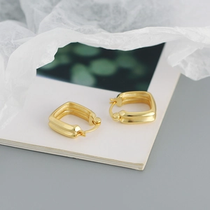 Close-up of elegant double-layered gold square huggie earrings on textured paper