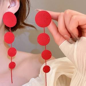 Detail of red tiered disc earrings with textured spiral patterns and long tassel design