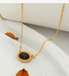 Macro view of vintage gold necklace with oval black stone on white silk fabric