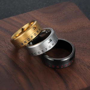 Titanium steel rotating alphabet ring in gold, silver, and black on a wood surface