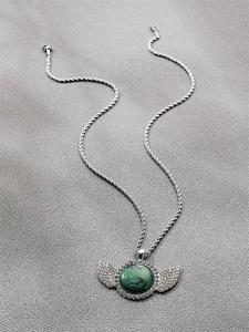 Détail du pendentif ailes argentées avec malachite verte et diamants sur tissu gris