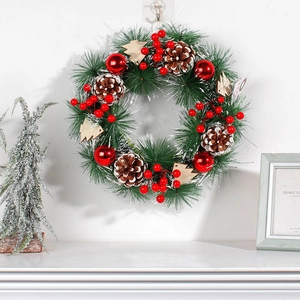 Christmas pine needle wreath with red berries and pine cones hanging on a white wall