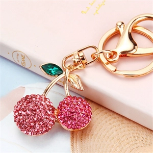 Llavero de cereza con cristales rosas y acabado dorado sobre fondo de libro decorativo