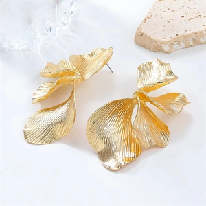 Detail shot of oversized gold leaf earrings with textured metallic finish on stone