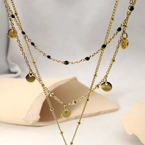 Detail of layered gold necklace with black beads and polished oval pendant charms