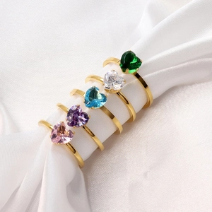 Close-up of five heart-shaped colorful gemstone rings on smooth white silk fabric