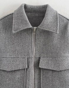 Détail d'une veste en laine grise avec col à revers, fermeture éclair et grandes poches
