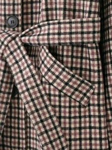 Close-up of vintage purple plaid coat showing wool texture, belt, and black button