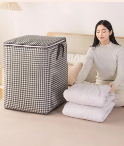 Detail of model folding a white quilt into a large houndstooth storage bag in a bedroom