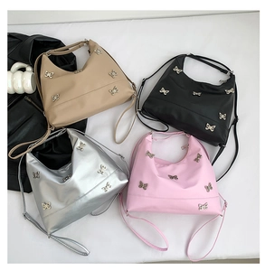 Flat lay of tote bags in khaki, black, silver, and pink featuring metal butterfly charms