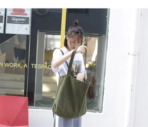 City outdoor shot of a casual green canvas tote bag being used by a model
