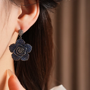 Detail of vintage silver needle earring with blue zircon rose flower on model ear