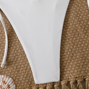 Detail of white bikini bottoms with thin ties on a textured straw mat with a seashell