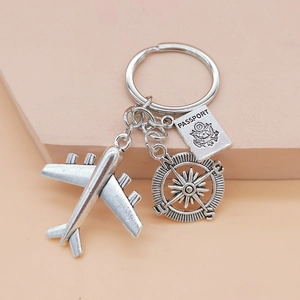 Detail of travel keychain with airplane, compass and passport charms on a pink stand