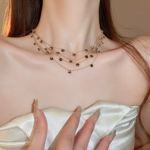 Detailaufnahme der mehrlagigen Goldhalskette mit dunklen Zirkonanhängern an einem Model
