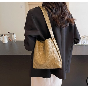 Detail of khaki woven bucket bag texture with wide shoulder strap on a model