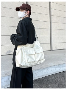 On-shoulder view of a large cream canvas bag with dual front pockets for daily commute
