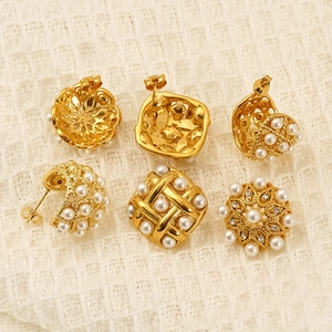 Three pairs of vintage gold titanium steel earrings with pearls and rhinestones on beige fabric