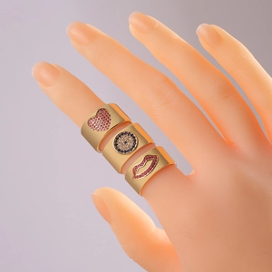Detail of three 18K gold plated wide rings with red heart, evil eye, and lip motifs