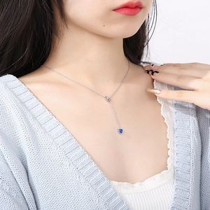 Close-up of model wearing silver Y-shaped heart necklace with blue sapphire pendant