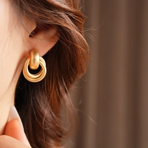 Macro shot of matte gold geometric double hoop earrings worn on a female ear