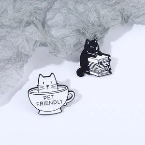 Cute cartoon cat pins set featuring a white cat in a cup and a black cat holding a book