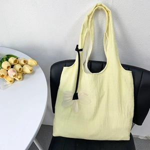 Detail of light yellow pleated canvas tote bag with black ribbon on a black chair