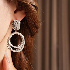 Detailed close-up of large silver layered concentric hoop earrings with hammered texture