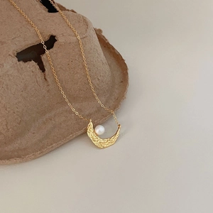 Detail of gold crescent moon necklace with irregular texture and white pearl accent