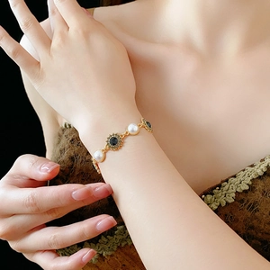 Close-up of vintage bracelet with white pearls and black sunflower charm on a golden chain