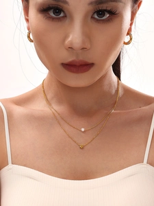 Close-up of layered 18K gold star and pearl necklace worn on model's neck