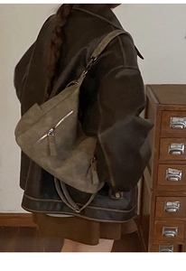 Retro khaki suede hobo bag on model's shoulder against a vintage wooden cabinet background