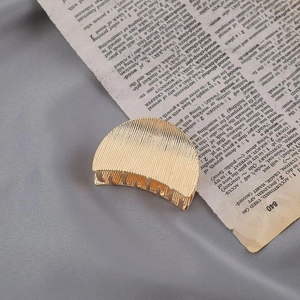 Detail of a golden metal hair claw clip with striped texture on a vintage book page