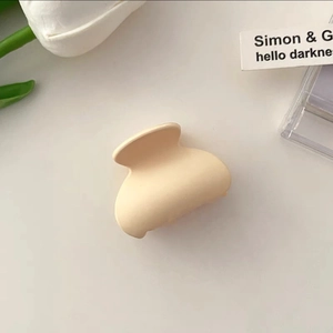 Detail shot of a small cream matte claw clip next to white tulips in a minimal setting