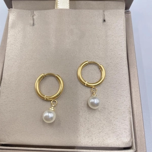 Elegant gold hoop earrings with white pearl pendants displayed on a beige silk cushion