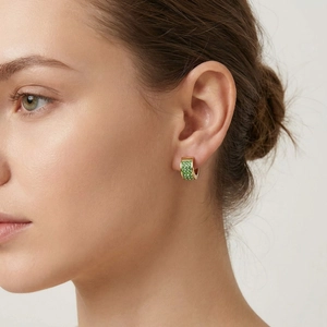 Close-up of a gold-plated ear hoop with green micro-paved crystals on a female model