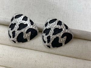 Macro shot of silver-tone irregular earrings with black animal print on fabric background