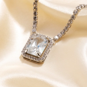 Elegant silver tennis necklace with a large rectangular zircon pendant on silk background
