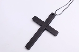 Close-up of black wooden cross pendant with a metallic bead chain on white background